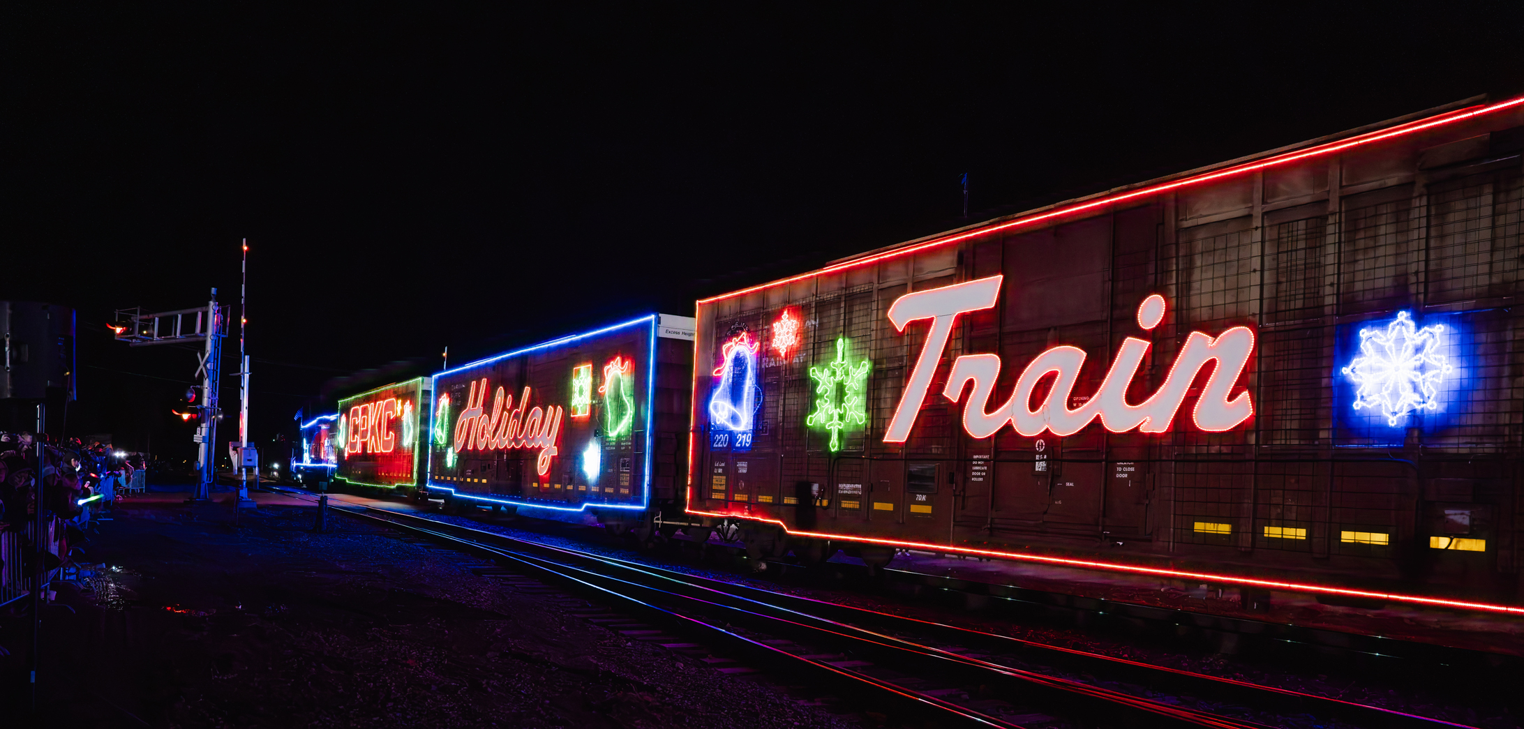Train cars lit up with neon lights spelling out "Holiday Train"