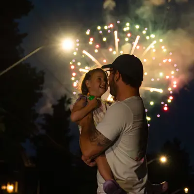 Father and daughter smiling with fireworks in background